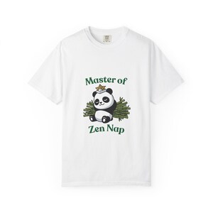 Może przedstawiać: Biała koszulka z kreskówkową pandą w kapeluszu w kształcie gwiazdy, odpoczywającą na bambusie. Tekst "Master of Zen Nap" jest wydrukowany na zielono nad i pod ilustracją pandy.