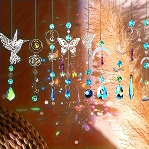 May include: A collection of hanging suncatchers featuring metal silhouettes of hummingbirds, butterflies, moons, and stars. Each piece is accented with colorful faceted glass beads and crystals in shades of blue, green, and purple, suspended on thin metal chains.