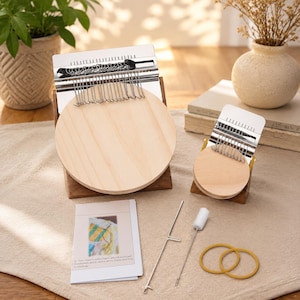 May include: Two wooden darning looms of different sizes with metal hooks and circular wooden bases, accompanied by a printed instruction manual, a metal needle tool, a small white brush, and two yellow rubber bands for textile repair.