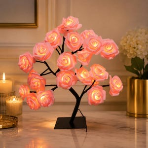 May include: A decorative tree lamp featuring numerous soft pink rose-shaped light fixtures attached to thin black branches. The structure is supported by a square black base, and each individual rose emits a warm, glowing light from its center.