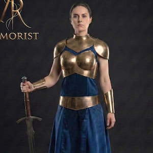 Könnte beinhalten: Eine Person in einem dunkelblauen Kleid mit goldfarbener Rüstung, einschließlich Brustpanzer, Schulterstücken und Armmanschetten, hält ein Schwert. Das Wort "ARMORIST" ist in Gold gedruckt.