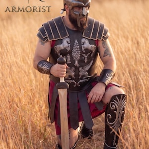 Könnte beinhalten: Ein dunkler Gladiatorenhelm mit Kamm, ein schwarzer Lederharnisch mit silberfarbenen Pferde- und Greifenreliefs, passende Armschienen und eine Beinschiene. Das Set umfasst ein Langschwert mit rundem Knauf und eine tiefrote Tunika.