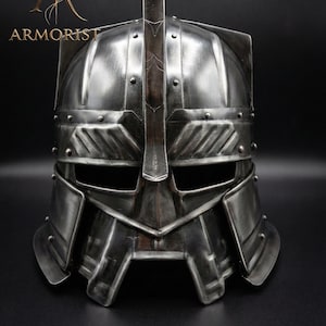 Peut inclure: Casque en métal argenté avec une crête centrale et une construction rivetée. Le casque comporte des ouvertures pour les yeux et un protège-visage détaillé. Le mot "ARMORIST" est visible.