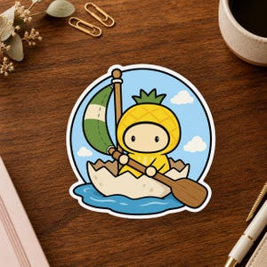 May include: A circular sticker featuring a cartoon character dressed in a yellow pineapple costume, sitting in a cracked white eggshell boat on blue water. The character holds a brown wooden paddle and a mast with a green and white sail.
