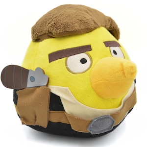 May include: A plush yellow Angry Birds character with brown eyebrows, a brown hat, and a yellow beak. The character has a brown holster with a silver tool. The character is wearing a black and tan outfit.