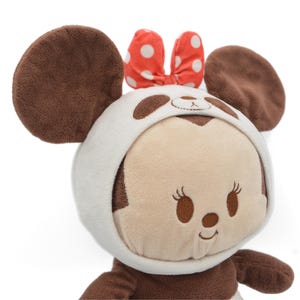 May include: A plush toy featuring a character with large brown ears and a white and brown panda-style hood. The character has a light brown face with embroidered features and a red bow with white polka dots.