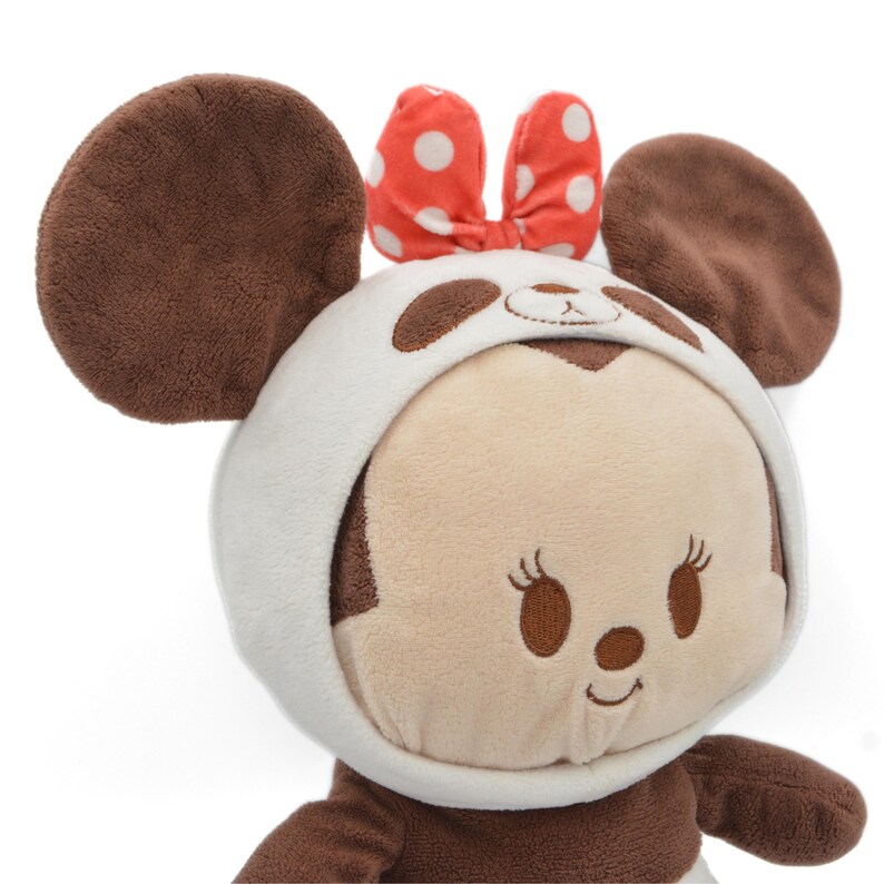 May include: A plush toy featuring a character with large brown ears and a white and brown panda-style hood. The character has a light brown face with embroidered features and a red bow with white polka dots.