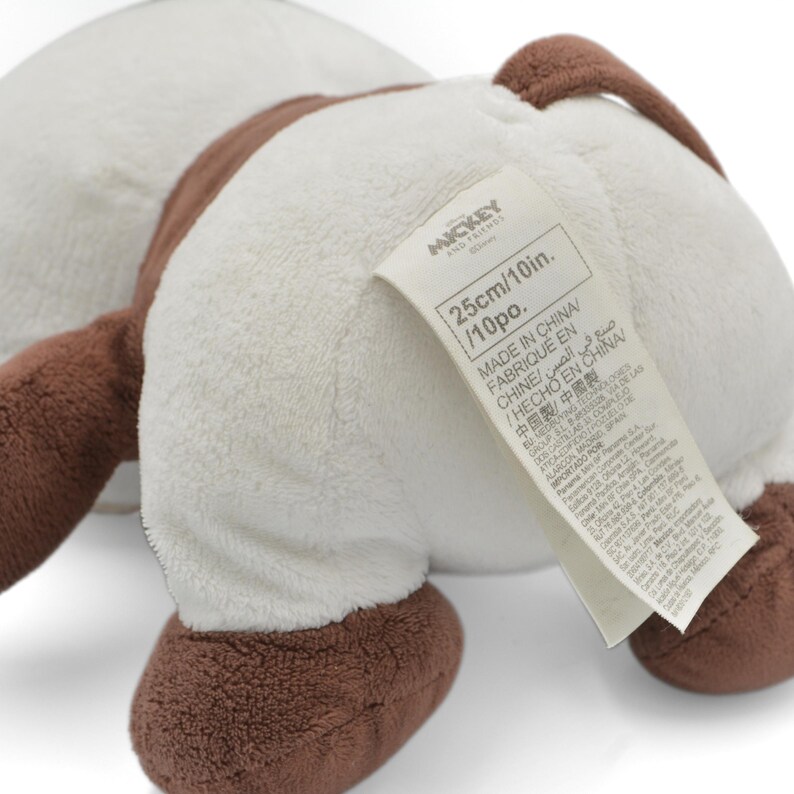 May include: A plush toy featuring a white body with brown accents. The toy has a tag that reads "MICKEY AND FRIENDS" and "25cm/10in.". The toy is made in China.