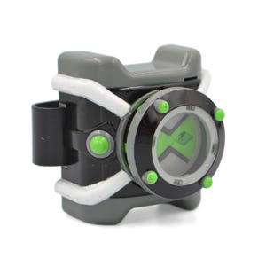 May include: A gray and black toy watch with white accents and a circular face. The watch features a bright green center with a black silhouette graphic, surrounded by a black bezel with four small green circular studs and a white frame structure.