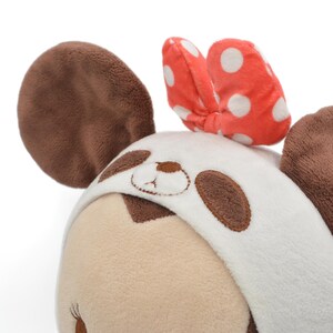 May include: A plush toy featuring a panda design. The toy has brown ears, a white and brown panda face, and a red bow with white polka dots. The toy is made of soft, plush material.