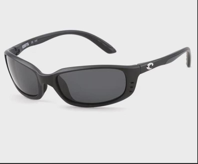 Puede incluir: Gafas de sol negras con lentes oscuras. Las gafas tienen una montura curvada y la marca "COSTA" es visible en la patilla izquierda. El logotipo de Costa est&aacute; en la patilla derecha.