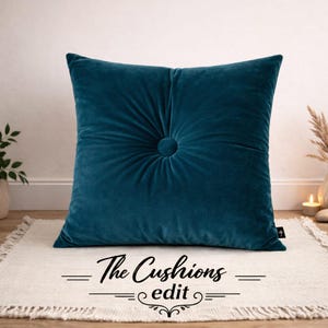 May include: A teal velvet cushion with a button center. The cushion is square and has a tufted design. The text "The Cushions edit" is at the bottom of the image.