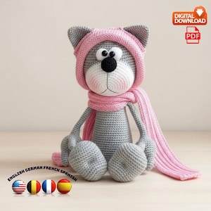 May include: A crocheted cat doll in grey, white, and pink. The cat wears a pink hat and scarf. The doll is sitting with its legs crossed. The image includes the text "DIGITAL DOWNLOAD PDF".