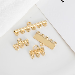 Könnte beinhalten: Goldfarbene Schmuckverschlüsse in verschiedenen Formen, darunter Stäbe und kettenartige Designs. Das Bild enthält auch eine weiße Karte mit dem Aufdruck "FALL IN LOVE".