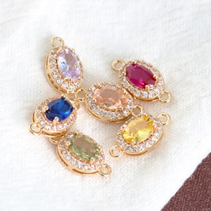 May include: Six gold-toned oval connectors with colorful gemstone centers. Each connector features a different gemstone color: purple, blue, peach, red, yellow, and green, surrounded by a halo of small, clear crystals.