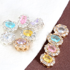 Pode incluir: Uma coleção de contas de pedras preciosas coloridas com engastes em prata e ouro. As contas apresentam gemas de corte oval em várias cores, incluindo azul, rosa, amarelo e transparente, rodeadas por pedras menores e transparentes.