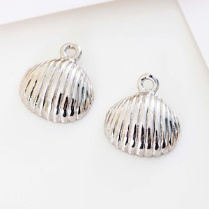 May include: Two silver seashell charms with a ridged texture. Each charm has a small loop at the top for attaching to jewellery. The charms are on a white background.