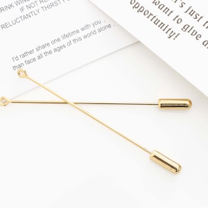 May include: Two gold-colored stick pins with rounded ends and small loops at the opposite end. The pins are lying on a white surface with text that reads, "I'd rather share one lifetime with you, than face all the ages of this world alone."