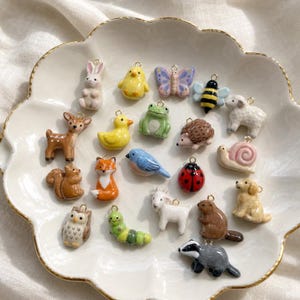 Peut inclure: Une collection de petites breloques en céramique représentant des animaux et des insectes, incluant un lapin, un poussin, un papillon, une abeille, un cerf, un canard, une grenouille, un hérisson, un mouton, un écureuil, un renard et une coccinelle.