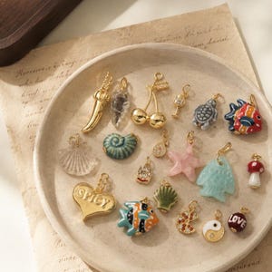 May include: A collection of assorted gold-toned metal and ceramic charms including a chili pepper, cherries, a turtle, a fish, a seashell, a heart with the word SPICY, a mushroom, a pizza slice, a yin-yang symbol, and a bead with the word LOVE.
