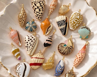 May include: A collection of assorted metal seashell charms featuring various enamel patterns, colors, and textures. Each charm includes a small gold-toned loop at the top for attachment, showcasing diverse shapes like conch, spiral, and bivalve shells.