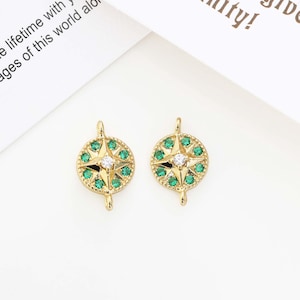 Peut inclure: Deux pendentifs ronds dorés avec un motif de rose des vents. Chaque pendentif présente une gemme blanche centrale entourée de gemmes vertes et d'un motif d'éclat d'étoile doré. Les pendentifs ont de petites boucles en haut et en bas.