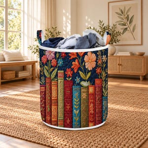 May include: A cylindrical fabric laundry hamper featuring a dark blue background with a quilted texture. The exterior displays a colourful print of vertical book spines in shades of red, green, and blue, topped with various orange and pink flowers.