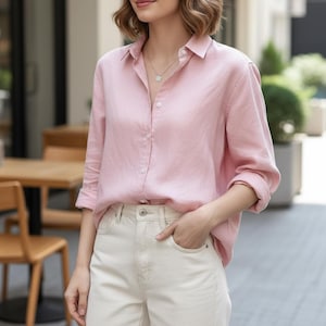 Pode incluir: Uma camisa rosa claro com botões, mangas compridas e gola. A camisa é combinada com jeans de ganga branco sujo. O conjunto é casual e adequado para o uso diário.