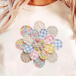 Op de afbeelding: Crèmekleurig T-shirt met een groot, geappliqueerd bloemdesign. De bloem heeft veelkleurige stoffen bloemblaadjes in bloemen-, ruit- en effen patronen, met een knoopcentrum. De bloemblaadjes zijn gestikt met rode draad.