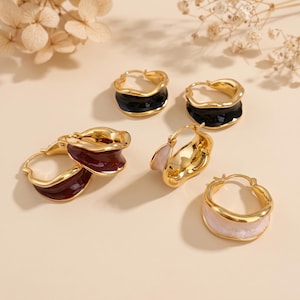 May include: A collection of hoop earrings featuring a gold-toned metal frame with a wavy, irregular edge. The earrings are available in various colors, including glossy black, deep burgundy, and a soft, marbled white finish on the inner surface.