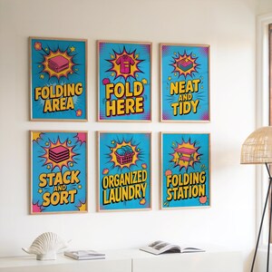 May include: Six framed laundry room art prints with a pop art style. Each print features a different laundry-related phrase in yellow text on a blue background, such as "Folding Area" and "Fold Here". The frames are light brown.