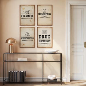 Könnte beinhalten: Vier gerahmte Schilder im Vintage-Stil mit den Texten "Apotheke", "Rezeptabholung", "Medikamente" und "Drogerie". Die Schilder hängen an einer beigefarbenen Wand über einem schwarzen Metallkonsolentisch.