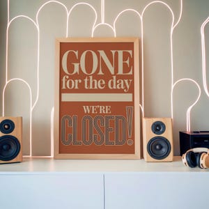 以下が含まれることがあります： 「GONE for the day WE'RE CLOSED!」という文字がレトロなフォントで書かれた額入りのサイン。白いキャビネットの上にあり、木製のスピーカー2つとヘッドホンが置かれています。