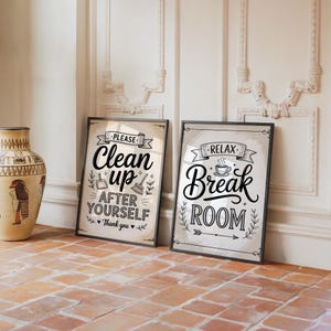 May include: Two framed signs with black borders lean against a wall. One sign reads "Clean up after yourself, thank you" in a vintage style. The other sign says "Relax, Break Room" with a coffee cup graphic. The signs are on a tiled floor.