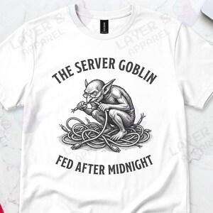 May include: White t-shirt with a graphic of a goblin sitting on cables, with the text "THE SERVER GOBLIN FED AFTER MIDNIGHT". The design is in black and white.
