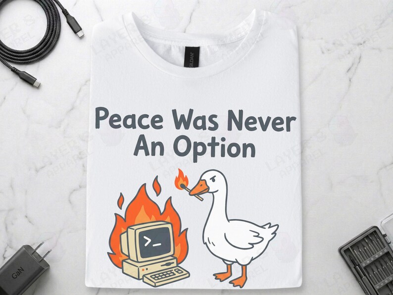 White Gildan t-shirt featuring a cartoon white goose holding a lit match next to a burning retro computer, with text "Peace Was Never An Option" and the Linux command "sudo rm -rf /".