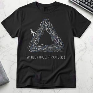 Black Gildan 64000 t-shirt featuring a Penrose impossible triangle made of tangled grey and white computer cables with a small white stick figure walking on it, above the white code text "WHILE (TRUE) { PANIC(); }".