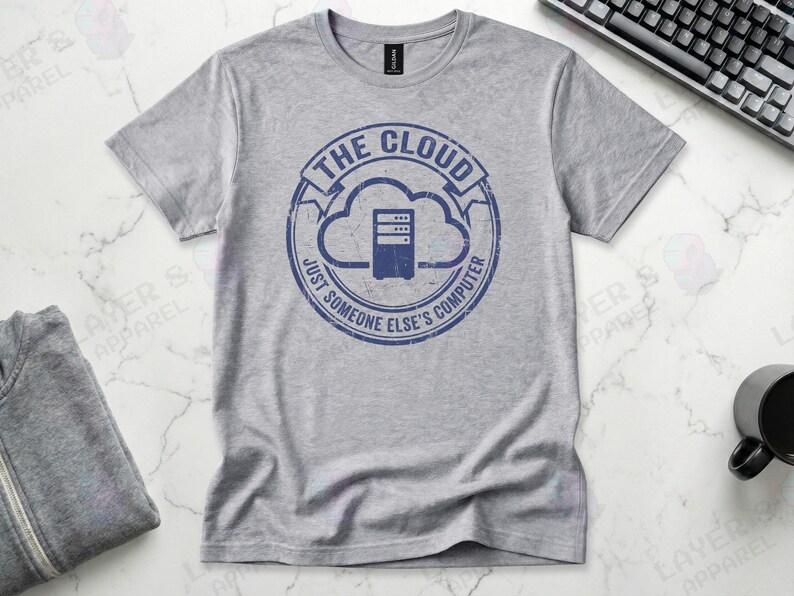 Sports grey t-shirt displaying a blue distressed stamp graphic. Text reads "THE CLOUD JUST SOMEONE ELSE'S COMPUTER" surrounding a server rack icon inside a cloud outline. A cynical technical definition of cloud infrastructure. Grunge vintage style.