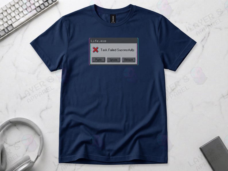 Navy blue t-shirt displaying a retro computer error window graphic with a glitch effect. Title bar reads "Life.exe" with a red X icon. Message reads "Task Failed Successfully." Buttons options are "Panic", "Ignore", and "Reboot." A humorous meme referencing contradictory system errors and existential anxiety.