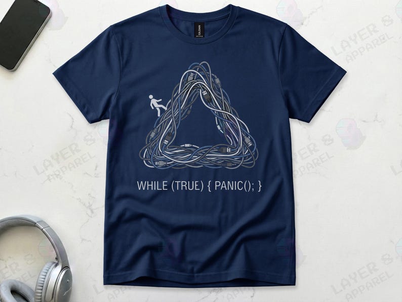 Navy blue Gildan 64000 t-shirt featuring a Penrose impossible triangle made of tangled grey and white computer cables with a small white stick figure walking on it, above the white code text "WHILE (TRUE) { PANIC(); }".