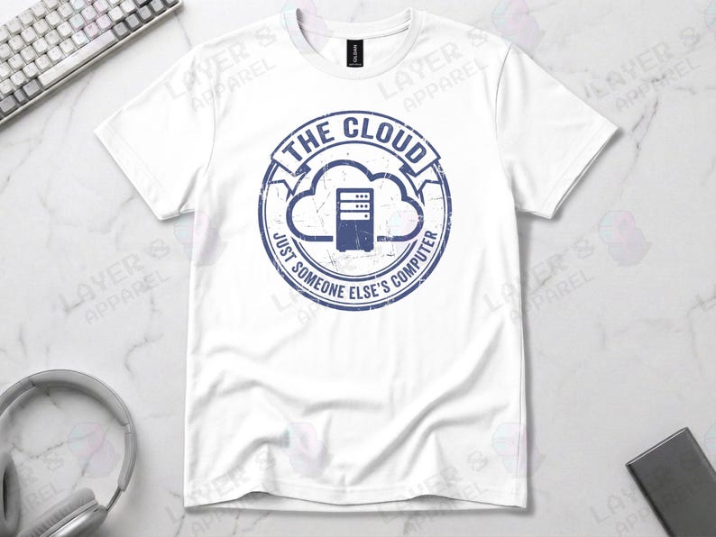 White t-shirt displaying a blue distressed stamp graphic. Text reads "THE CLOUD JUST SOMEONE ELSE'S COMPUTER" surrounding a server rack icon inside a cloud outline. A cynical technical definition of cloud infrastructure. Grunge vintage style.