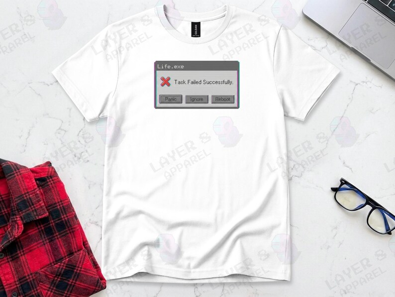 White t-shirt displaying a retro computer error window graphic with a glitch effect. Title bar reads "Life.exe" with a red X icon. Message reads "Task Failed Successfully." Buttons options are "Panic", "Ignore", and "Reboot." A humorous meme referencing contradictory system errors and existential anxiety.