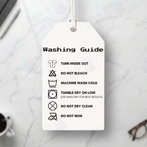 May include: A white tag displaying a washing guide with symbols for turning inside out, no bleach, cold machine wash, tumble dry on low, no dry cleaning, and no ironing. The tag is suspended by a white string.
