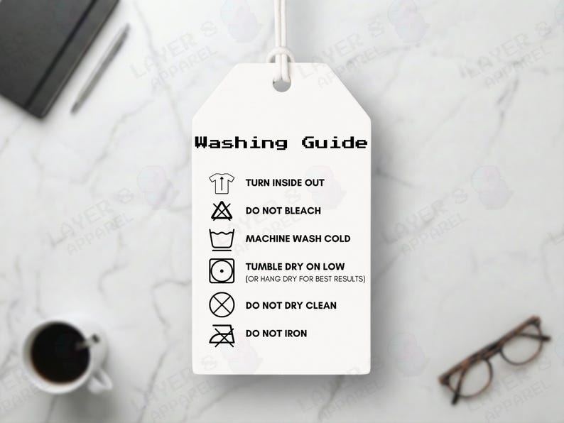 May include: A white tag displaying a washing guide with symbols for turning inside out, no bleach, cold machine wash, tumble dry on low, no dry cleaning, and no ironing. The tag is suspended by a white string.