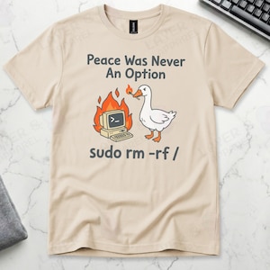 Sand Gildan t-shirt featuring a cartoon white goose holding a lit match next to a burning retro computer, with text "Peace Was Never An Option" and the Linux command "sudo rm -rf /".