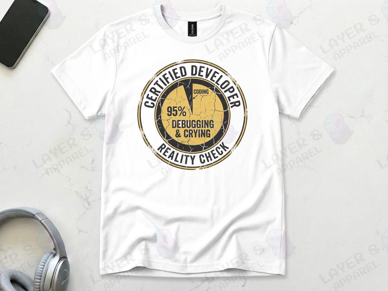 White t-shirt displaying a distressed circular badge graphic. Text reads "CERTIFIED DEVELOPER REALITY CHECK" surrounding a pie chart where 95% is labeled "DEBUGGING & CRYING" and a tiny sliver is "CODING". A humorous grunge-style statistic about the coding profession.