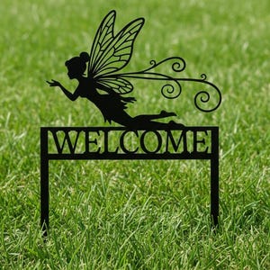 May include: Black metal garden stake with a fairy silhouette and the word "WELCOME". The fairy has detailed wings and is positioned above the text. The stake is designed for outdoor use in a garden or lawn.