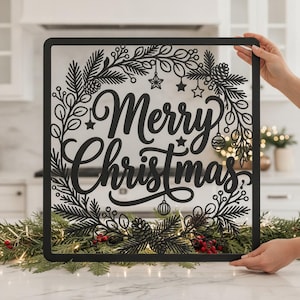 Könnte beinhalten: Ein quadratisches Wandbild aus schwarzem Metall mit dem Schriftzug Merry Christmas in Schreibschrift. Der Text ist von einem dekorativen, lasergeschnittenen Kranz aus Tannenzweigen, Tannenzapfen, kleinen Sternen und Ornamenten umgeben.