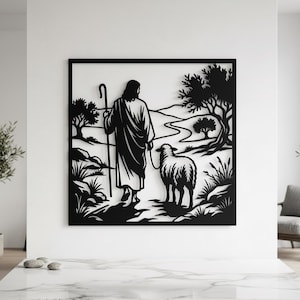 Könnte beinhalten: Ein Wandkunstobjekt aus schwarzem Metall mit einer Silhouette einer in Roben gekleideten Figur, die einen Stab hält und ein Schaf auf einem Pfad durch eine Landschaft mit Bäumen und Hügeln führt, eingefasst in einen quadratischen Rahmen.