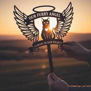 Könnte beinhalten: Schwarzer Katzen-Gedenkpfahl aus Metall mit Engelsflügeln, Heiligenschein und dem Text "OUR FURRY ANGEL" und "ALWAYS IN OUR HEARTS". Die Katzensilhouette hat einen herzförmigen Ausschnitt. Vor einem Sonnenuntergangshintergrund.
